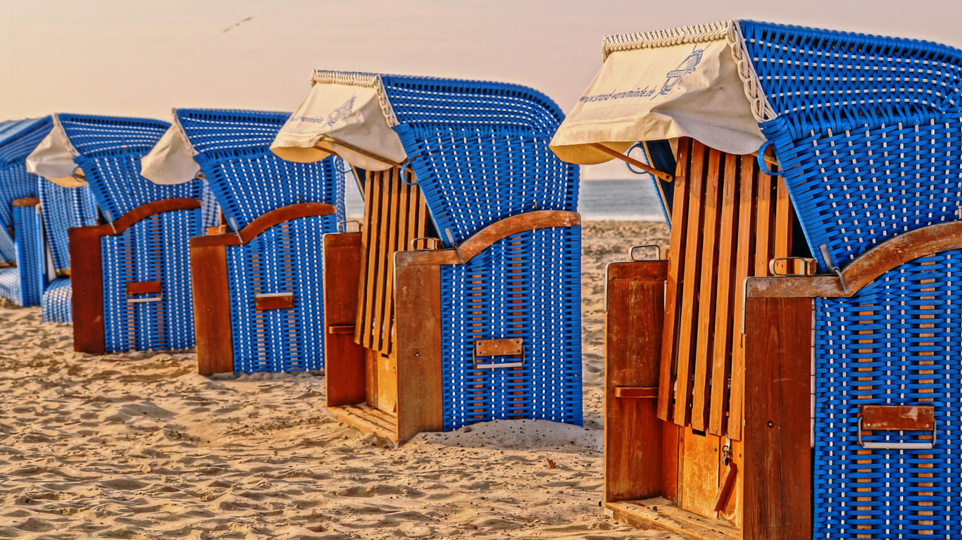 Blaue Strandkörbe stehen im Sand und warten auf einen ruhigen Tag am Meer.
