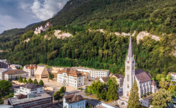 Panorama über eine Stadt mit Bergen und Wolken am Horizont.