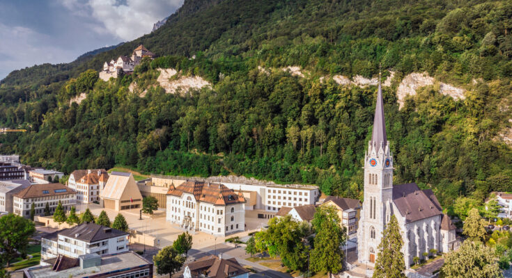 Panorama über eine Stadt mit Bergen und Wolken am Horizont.
