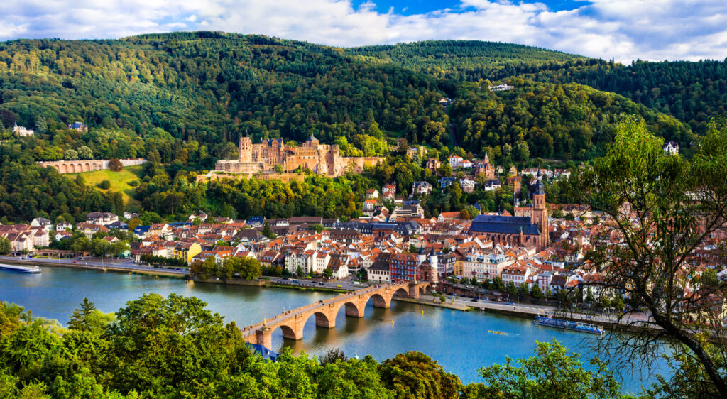 Ein weiter Blick über den Neckar mit der Alten Brücke hinweg auf die Heidelberger Altstadt und das Schloss am Hang.