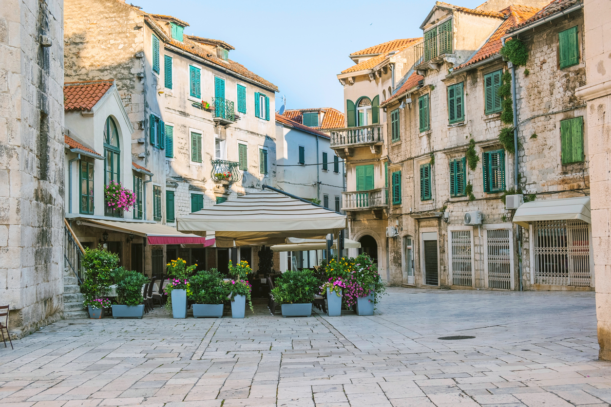 Ruhiger Altstadtplatz in Split mit Cafétischen, alten Steinmauern und grünen Fensterläden.