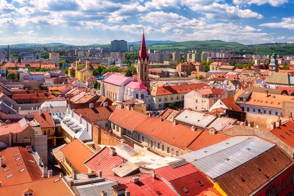 Blick über Košice mit roten Ziegeldächern, Kirchturmspitze und moderner Skyline am Horizont.