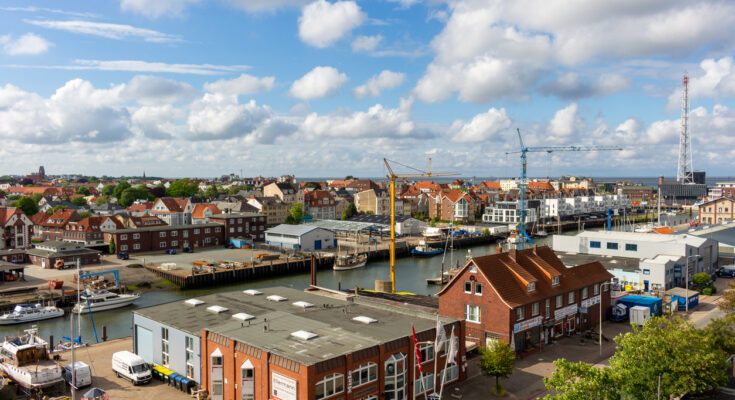 Eine erhöhte Ansicht auf Hafenbecken, Lagerhallen und Backsteingebäude unter einem leicht bewölkten Himmel.