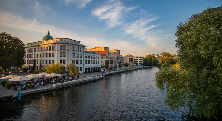 Klassische helle Gebäude und Cafés mit Sonnenschirmen säumen das ruhige Ufer der Havel unter einem weiten Abendhimmel.