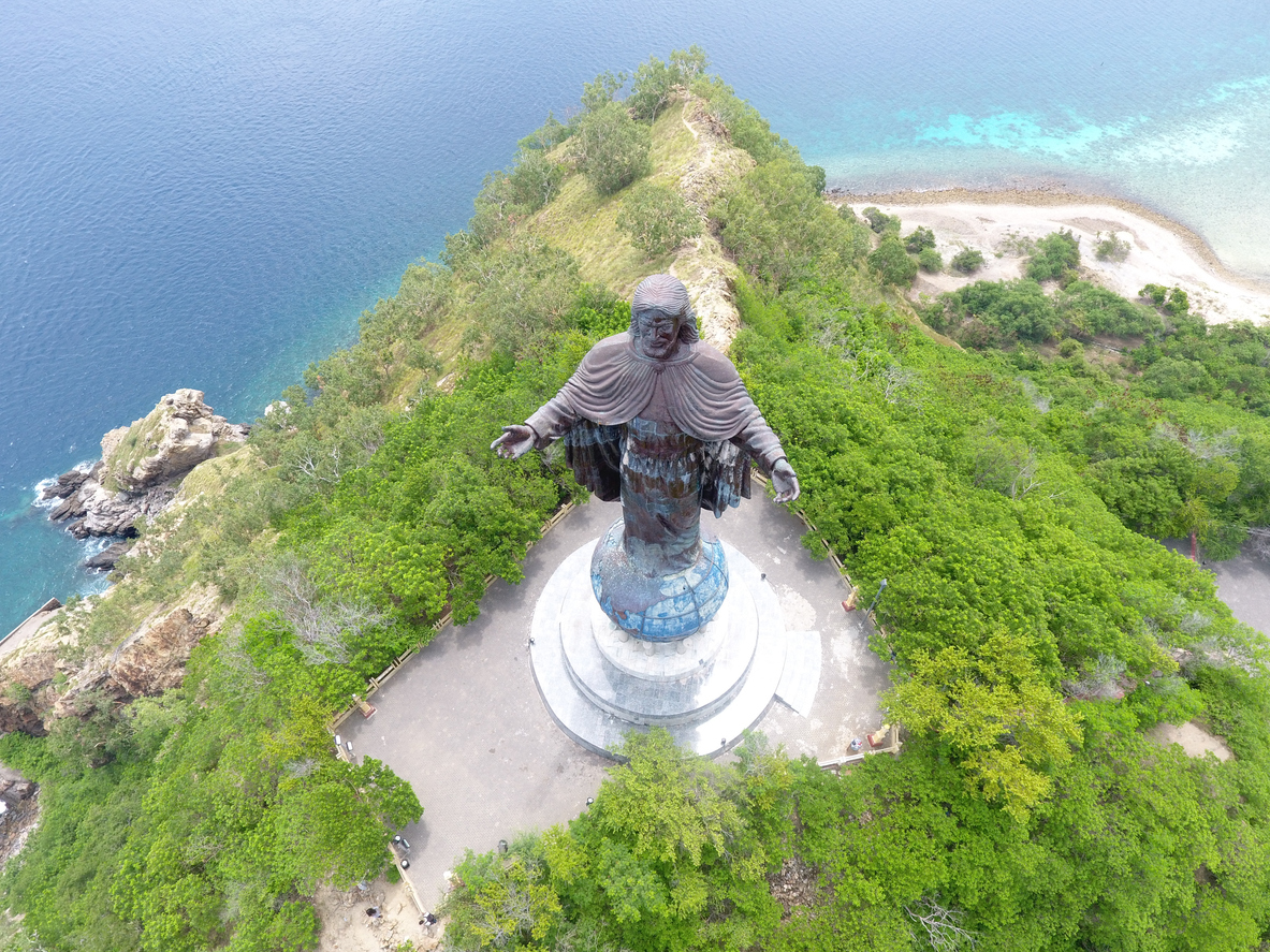 In Osttimor steht eine große Christusstatue auf einer Anhöhe, umgeben von Wald und Meerblick.