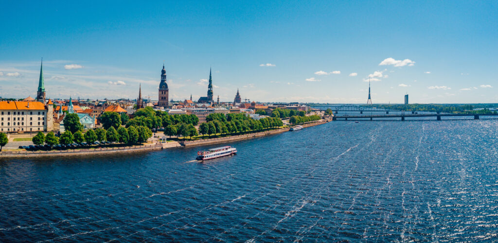 Ein Ausflugsboot fährt auf der glitzernden Daugava vor der historischen Silhouette der Stadt.