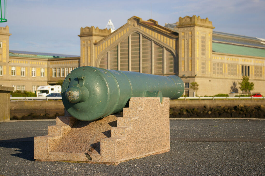 Eine alte grüne Kanone auf einem Steinsockel steht vor dem monumentalen Gebäude der Cité de la Mer.