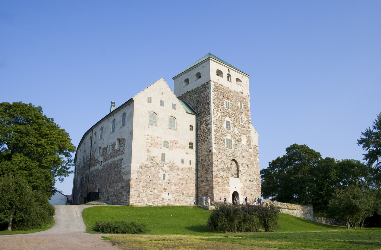 Die massive Steinfassade der Burg von Turku thront auf einem grünen Hügel unter einem strahlend blauen Himmel.
