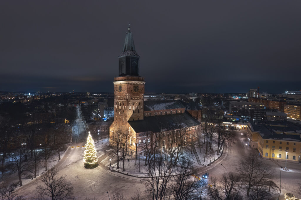 Nächtliche Aufnahme der Kathedrale von Turku im Winter mit einem hell erleuchteten Weihnachtsbaum auf dem verschneiten Vorplatz.