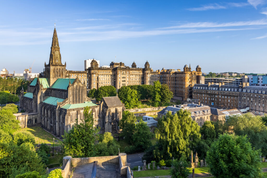 Blick von oben auf eine große gotische Kathedrale mit grünem Kupferdach, umgeben von Bäumen und historischen Gebäuden unter einem blauen Himmel.