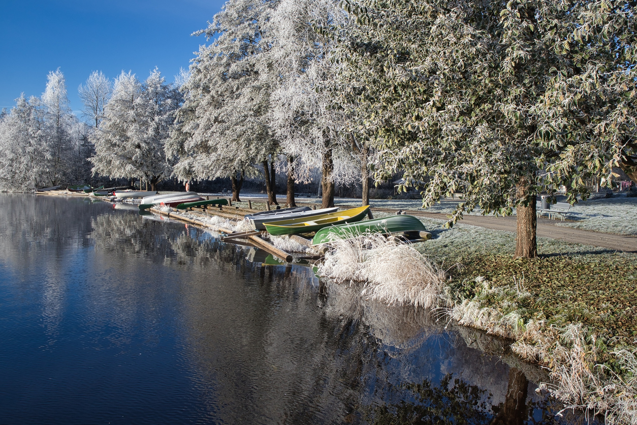Frostige Bäume, ruhiges Wasser und mehrere Boote am Ufer eines Flusses oder Kanals in Oulu.