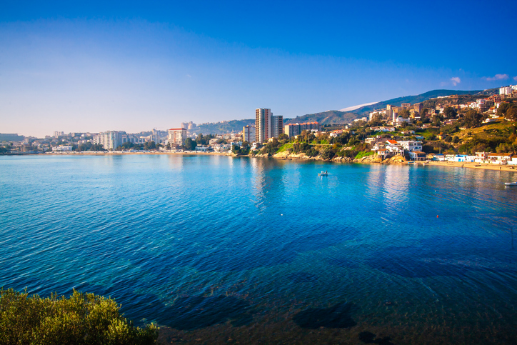 Eine weite Bucht mit kristallklarem, blauem Wasser und einer modernen Skyline im Hintergrund unter strahlendem Himmel.