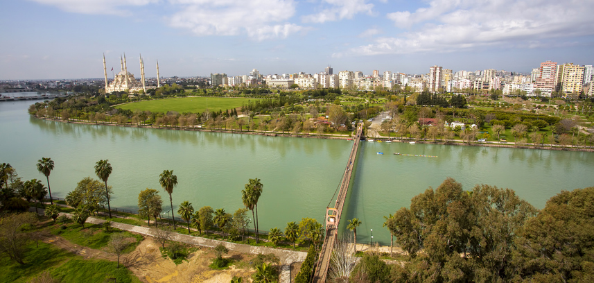 Eine weite Panoramaaufnahme zeigt die monumentale Moschee mit sechs Minaretten an einem breiten Fluss, der von einer Brücke überquert wird.