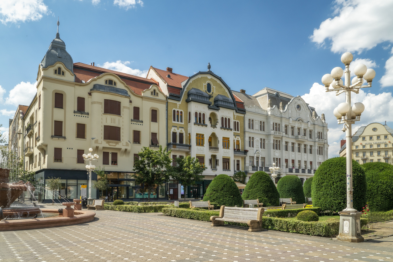 Eine Reihe von prächtig verzierten, mehrstöckigen Wohnhäusern mit Türmchen und Giebeln säumt einen gepflasterten Gehweg mit Sitzbänken.