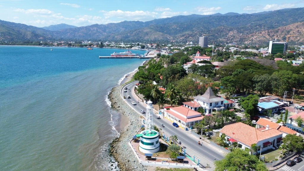 Küstenstraße mit Leuchtturm und Gebäuden entlang einer Bucht, aufgenommen aus der Luft.