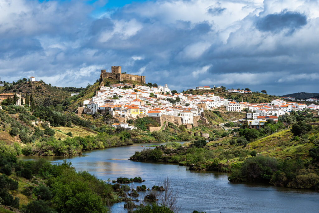 Weißes Hügeldorf mit Burganlage über einem Fluss in der Landschaft des Alentejo.