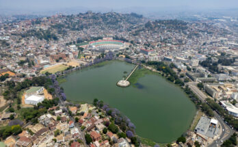 Eine Luftaufnahme zeigt den Lac Anosy im Vordergrund, dahinter erstrecken sich die dicht bebauten Hügel der Stadt bis zum Horizont.