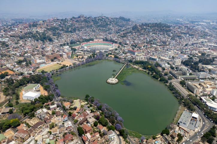 Eine Luftaufnahme zeigt den Lac Anosy im Vordergrund, dahinter erstrecken sich die dicht bebauten Hügel der Stadt bis zum Horizont.