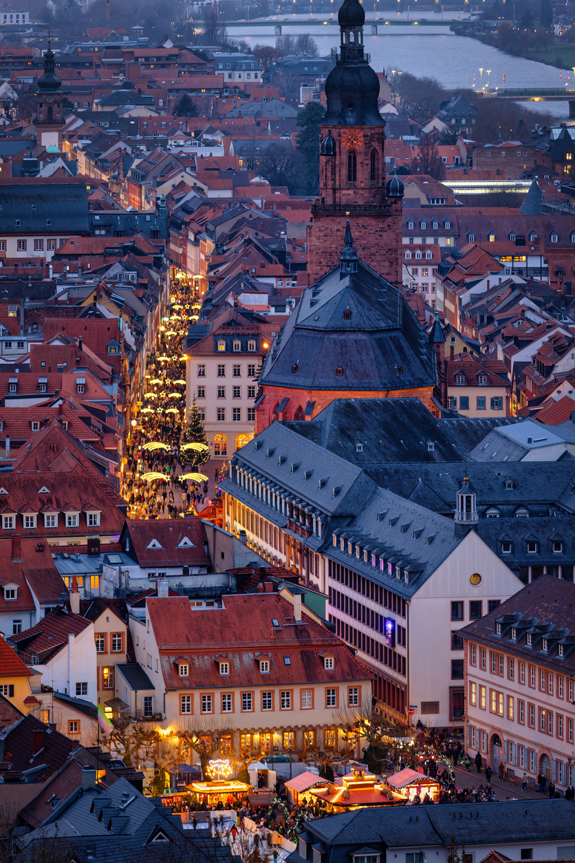 Eine Luftaufnahme der Heidelberger Altstadt in der Abenddämmerung mit der hell erleuchteten Fußgängerzone.