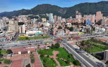 Ein Blick von oben auf eine breite Hauptstraße mit roten Gelenkbussen vor der Skyline von Bogotá und den Anden.