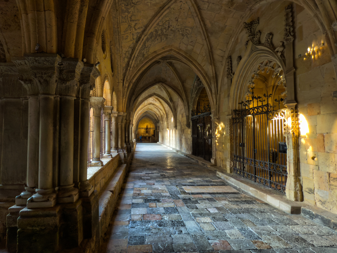 Ein schattiger Säulengang mit spitz zulaufenden Bögen und verzierten Kapitellen führt um einen hellen Innenhof.