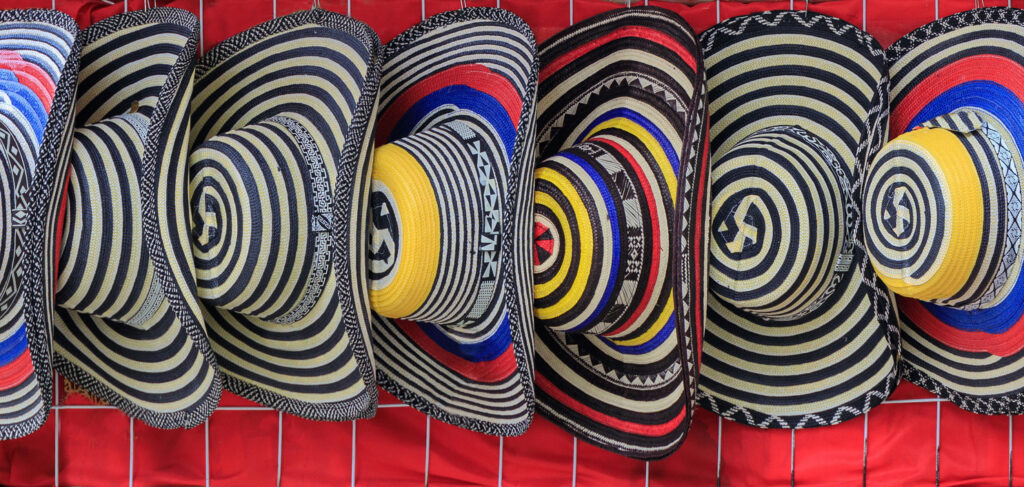 Eine Reihe von handgeflochtenen Hüten mit schwarz-weißen geometrischen Mustern hängt an einer roten Wand.