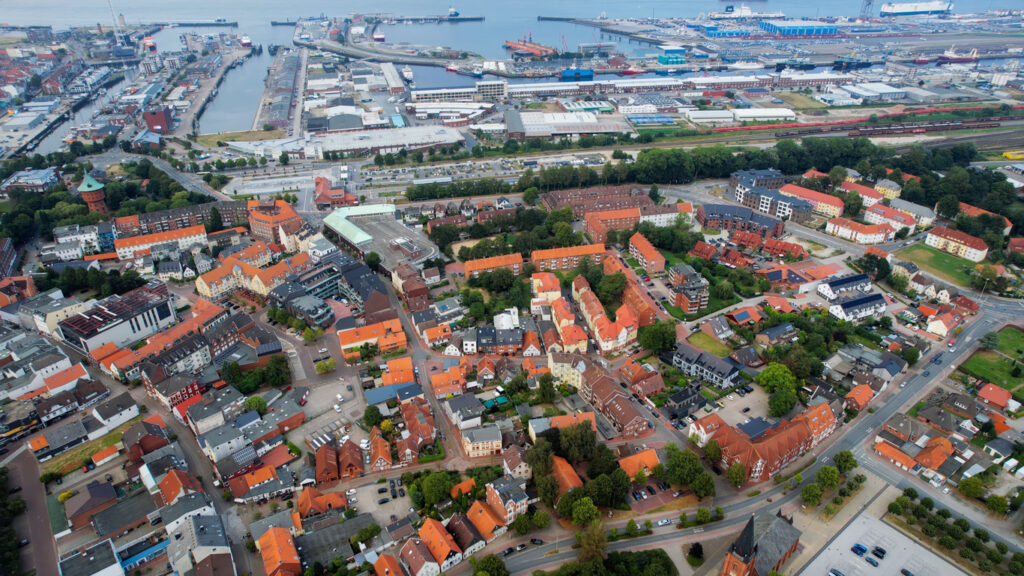 Eine weite Ansicht aus der Vogelperspektive zeigt die roten Hausdächer der Stadt, die bis an die Hafenbecken reichen.