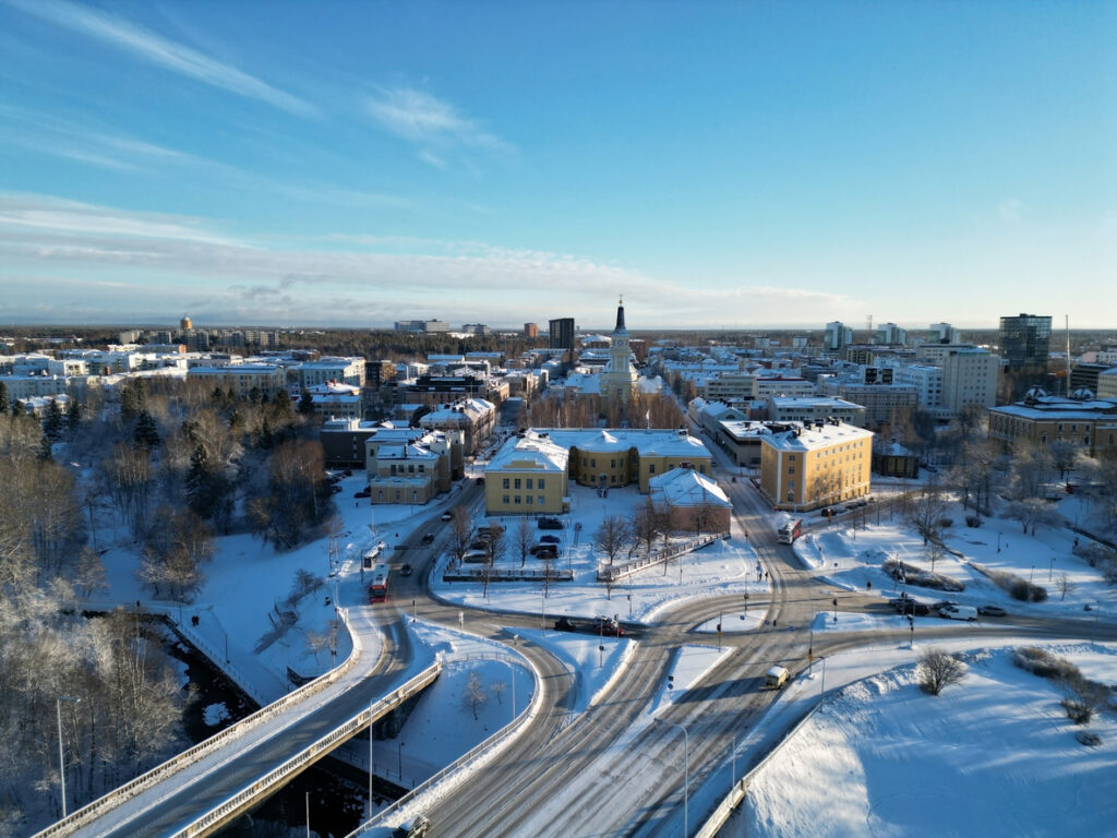 Luftaufnahme von Oulu im Winter mit verschneiten Straßen, Brücke, Flusslauf und Gebäuden im Stadtzentrum.