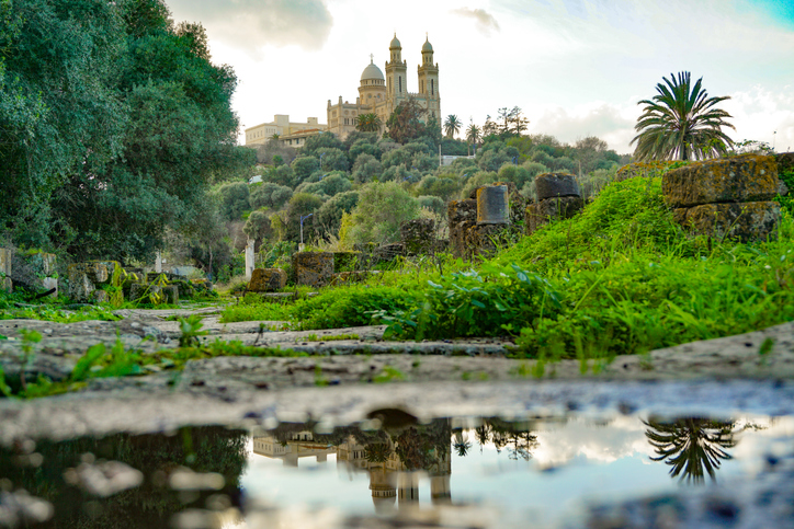 Die Basilika Saint-Augustin spiegelt sich in einer Wasserpfütze vor den antiken Ruinen von Hippo Regius.