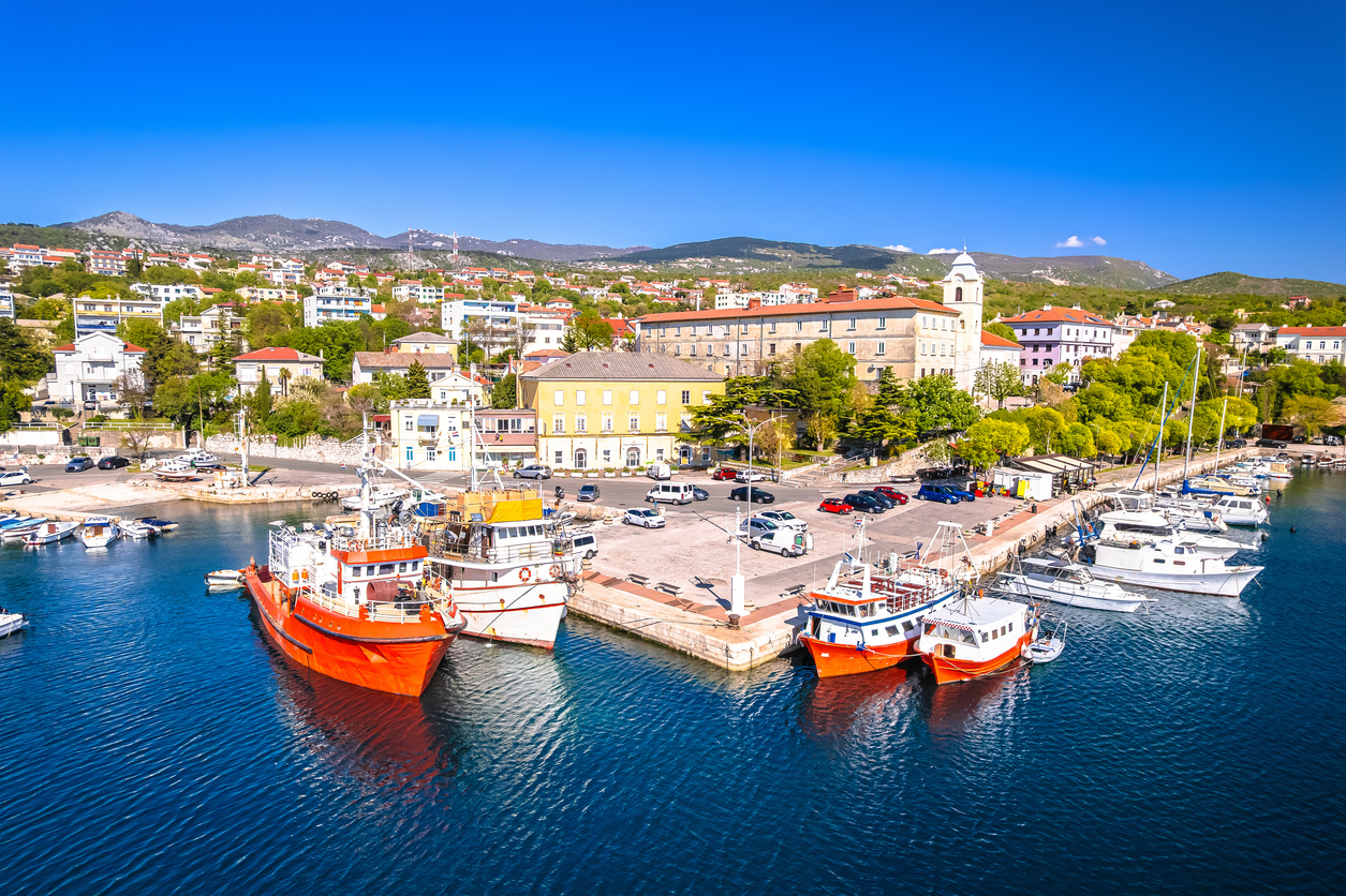 Blick auf einen Küstenort mit Booten im Hafen und blauem Wasser in der Kvarner-Bucht.