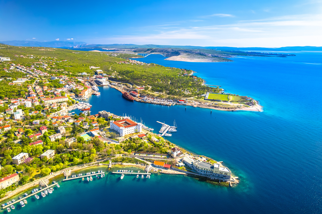 Luftaufnahme einer weit geschwungenen Küste mit Hafen, Booten und türkisblauem Meer in der Kvarner-Bucht.