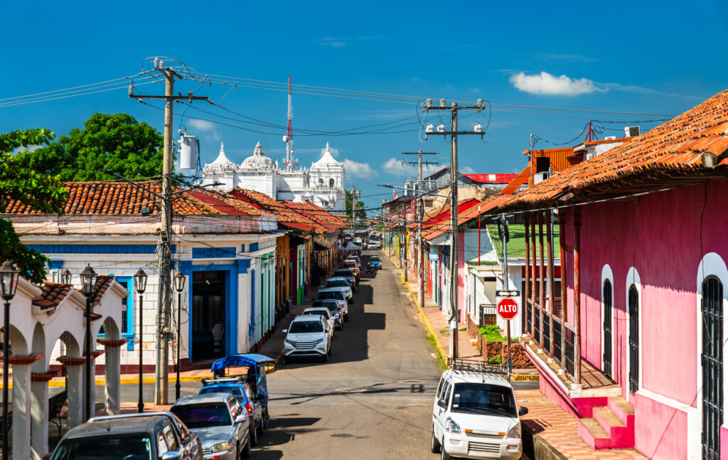 Straße mit bunten Häusern, parkenden Autos und Blick auf eine weiße Kirche in Nicaragua.