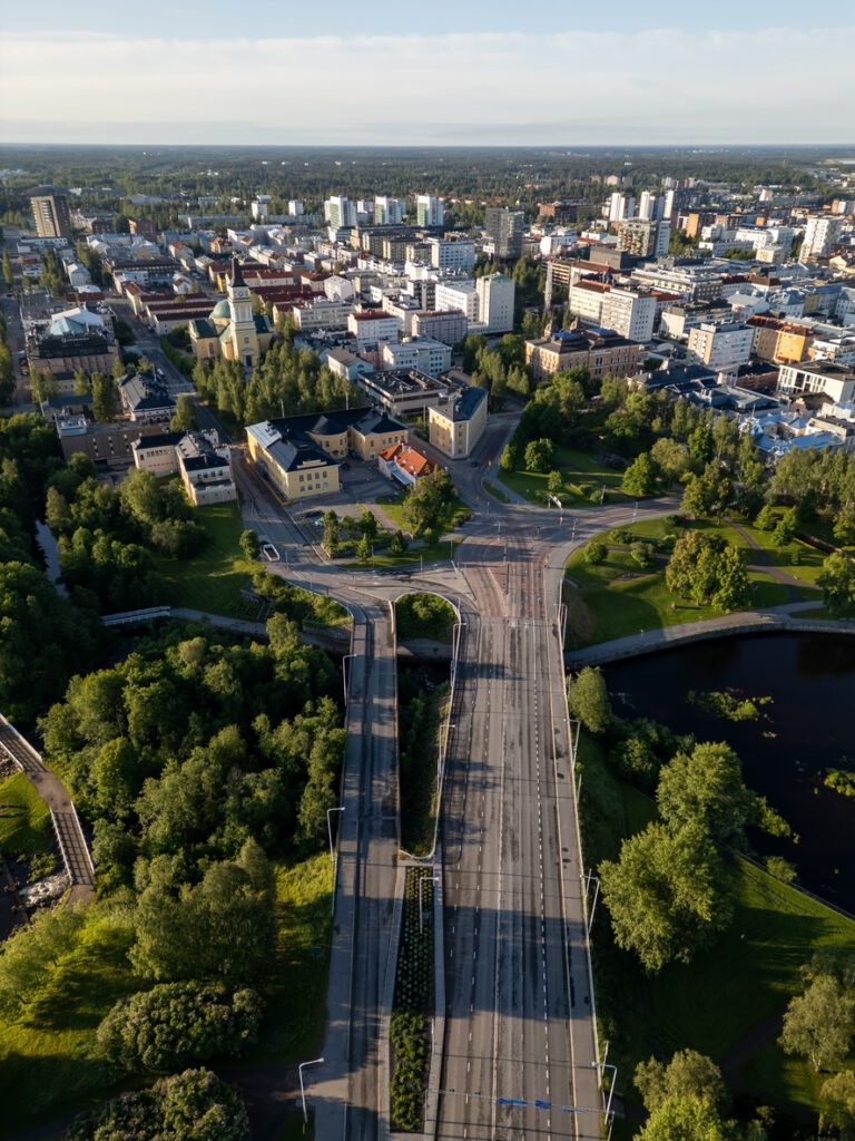 Drohnenaufnahme von Oulu mit breiter Straße, Flussarmen, Parks und dichter Bebauung im Hintergrund.