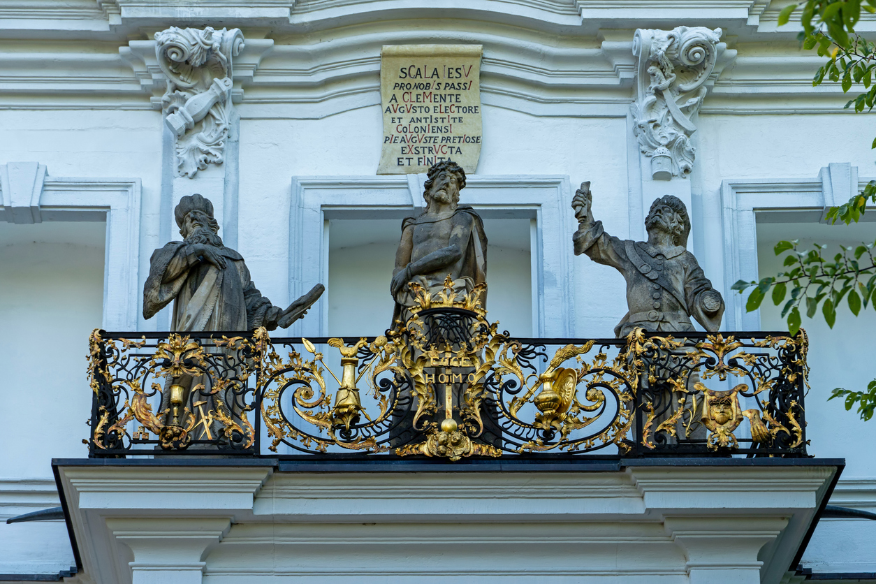 Ein prachtvoller Balkon mit vergoldetem Schmiedeeisengitter zeigt drei Steinstatuen – in der Mitte Christus als „Ecce Homo“.