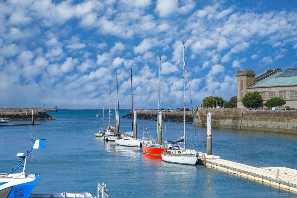 Mehrere Segelmasten ragen an einem Steg in den blauen Himmel, im Hintergrund ist das monumentale Museumsgebäude zu sehen.
