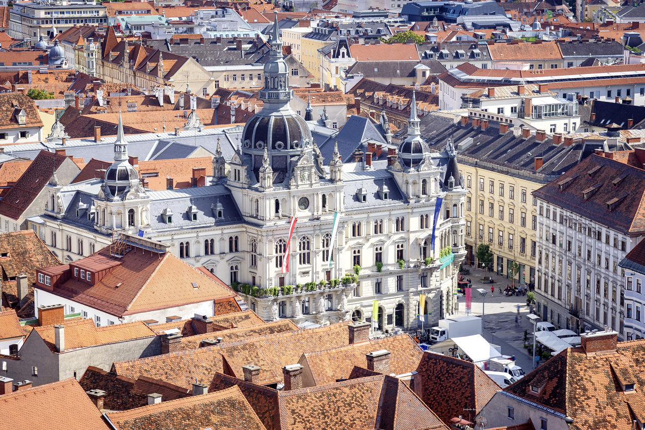 Blick von oben auf das monumentale Rathaus von Graz, das von der berühmten UNESCO-geschützten Dachlandschaft der Altstadt umgeben ist.