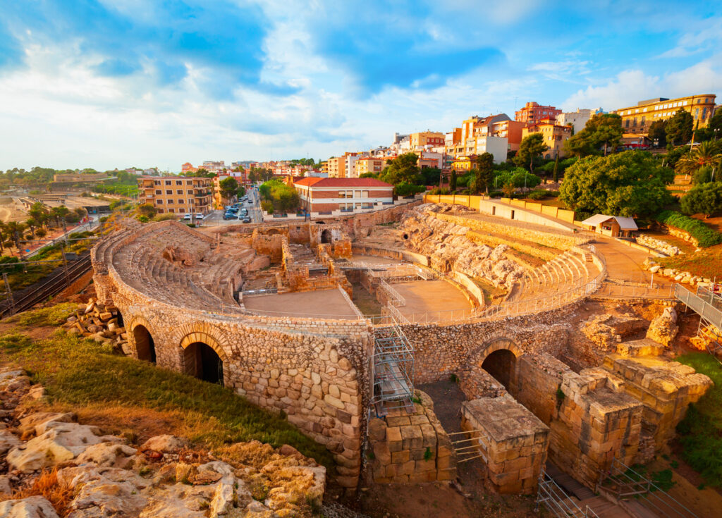 Ein Blick von oben auf die gut erhaltenen Grundmauern und Sitzreihen des Amphitheaters, eingebettet in die moderne Stadtstruktur.
