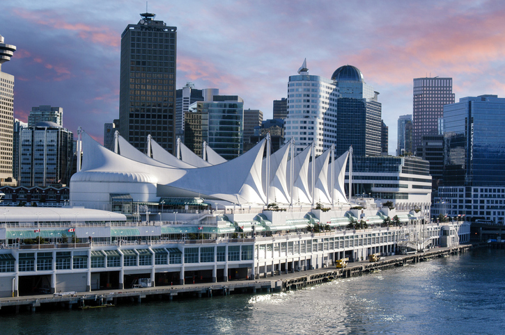 Die weißen segelförmigen Dächer des Canada Place ragen vor der Skyline von Vancouver in den rosa-blauen Abendhimmel.