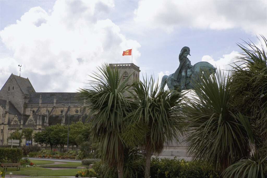 Eine Reiterstatue von Napoleon Bonaparte steht vor Palmen und dem Turm der Basilika Sainte-Trinité.