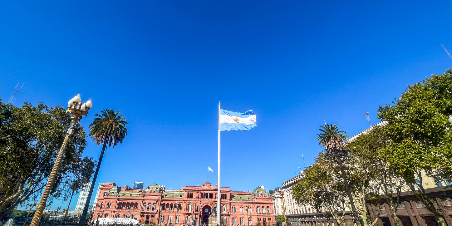 Die argentinische Flagge weht an einem hohen Mast im Zentrum von Buenos Aires vor der markanten Fassade der Casa Rosada.