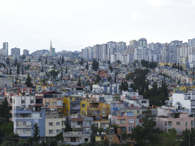 Ein Blick über bunte Wohnhäuser in der Unterstadt hinweg auf die moderne Skyline und das Minarett einer Moschee am Horizont.