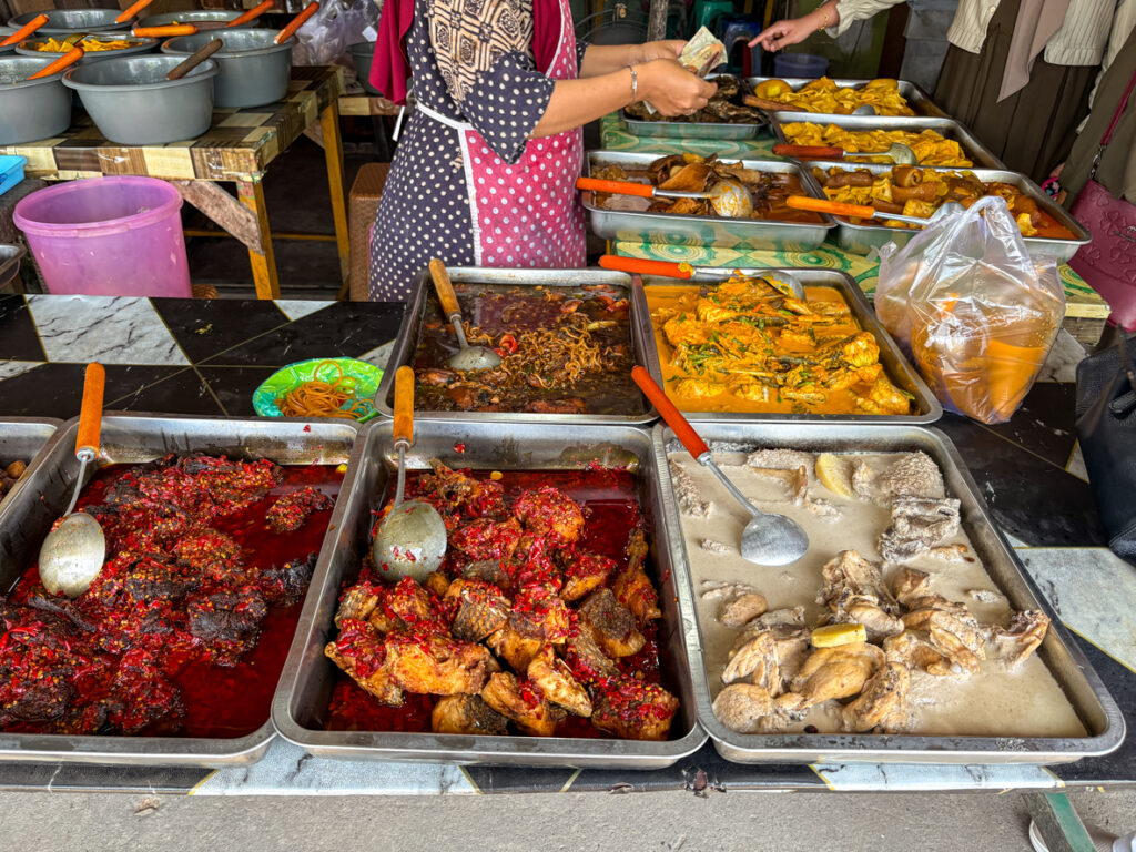 Verschiedene Schalen mit scharfen indonesischen Gerichten stehen auf einem Verkaufstisch im Freien.