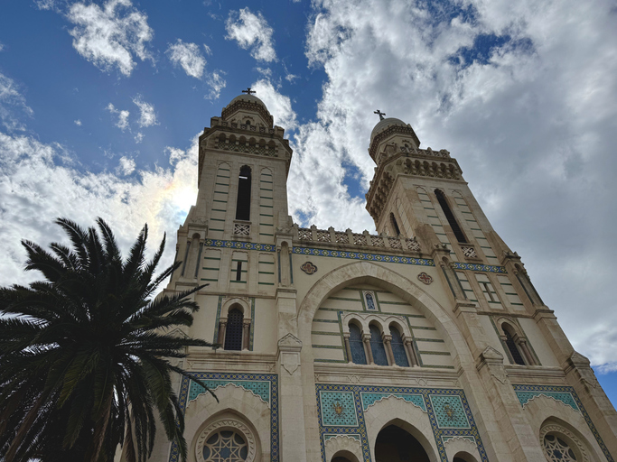 Die hellen Doppeltürme der Basilika Saint-Augustin ragen unter einem dramatischen, bewölkten Himmel empor.