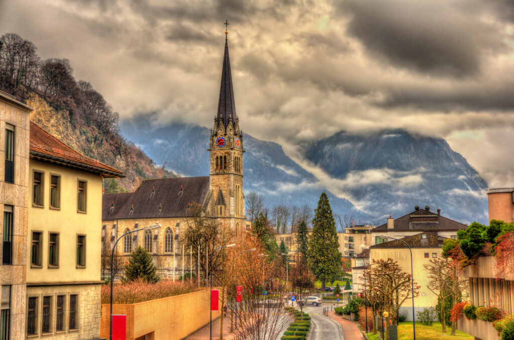 Große Kirche mit hohem Turm vor Bergen und dunklen Wolken.