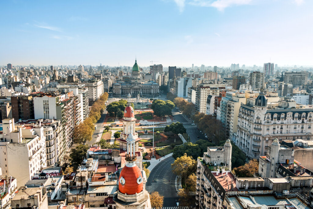 Eine urbane Panoramaaufnahme von Buenos Aires mit historischen Kuppelbauten im Vordergrund und dem Nationalkongress am Ende einer Allee.