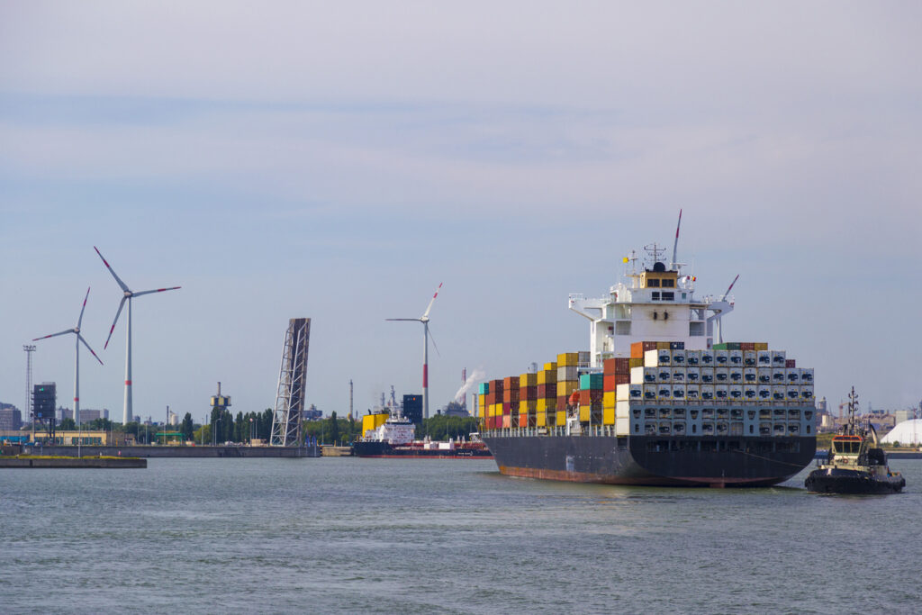 Großes Containerschiff im Hafenbecken mit Windrädern und Kränen in Antwerpen.