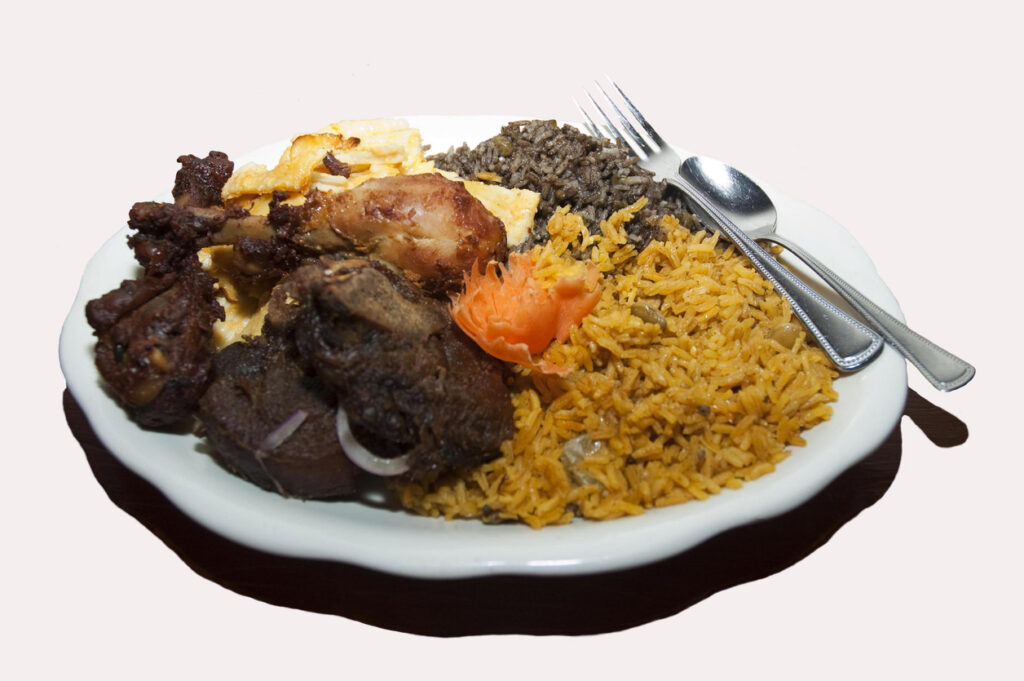 Ein reichhaltig beladener Teller mit haitianischem Reis und Bohnen, gebratenem Hähnchen und Beilagen.