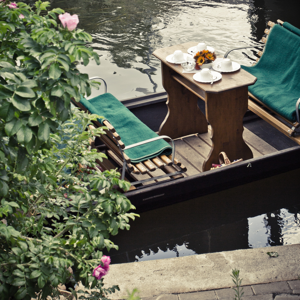 Kleines Boot mit Liegestühlen und Tischgeschirr liegt am Ufer eines Kanals.
