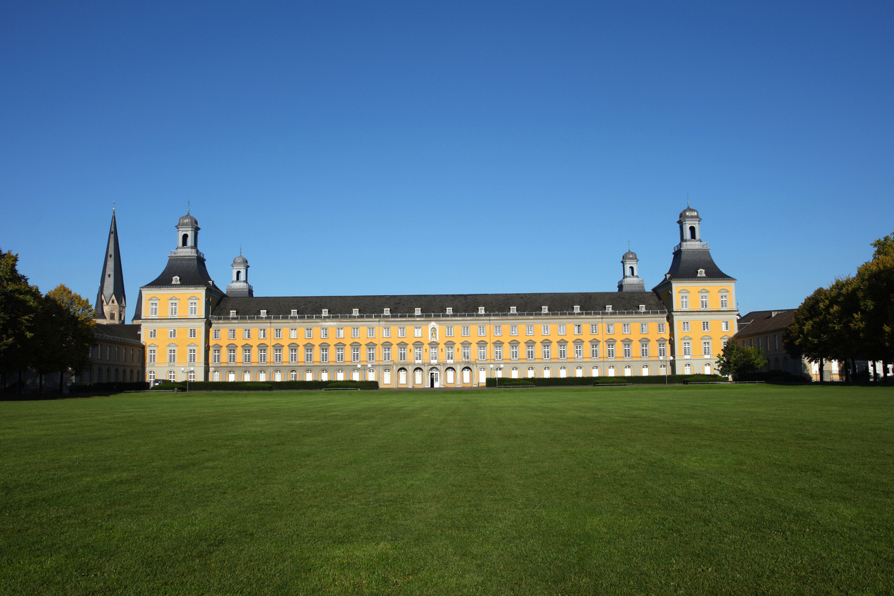 Die langgestreckte, gelbe Fassade des Schlosses mit seinen Eckturm-Pavillons erstreckt sich hinter einer weiten, grünen Rasenfläche (Hofgarten).