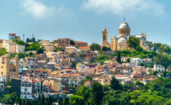Blick über dicht bebaute Hügel in Algier mit auffälliger Basilika und grünen Hängen.